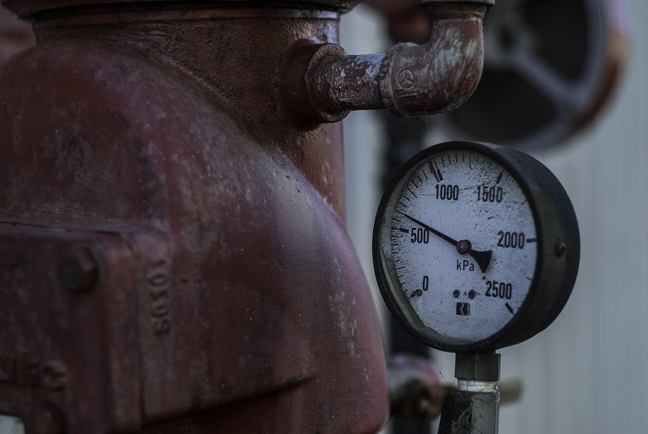 Close-up of a round analog water pressure gauge mounted on household plumbing pipes.