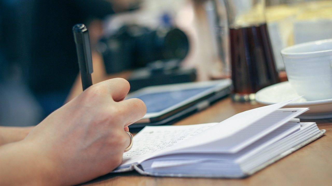 A peaceful household desk setup with a notebook, budget notes, and a digital banking app on a smartphone screen.