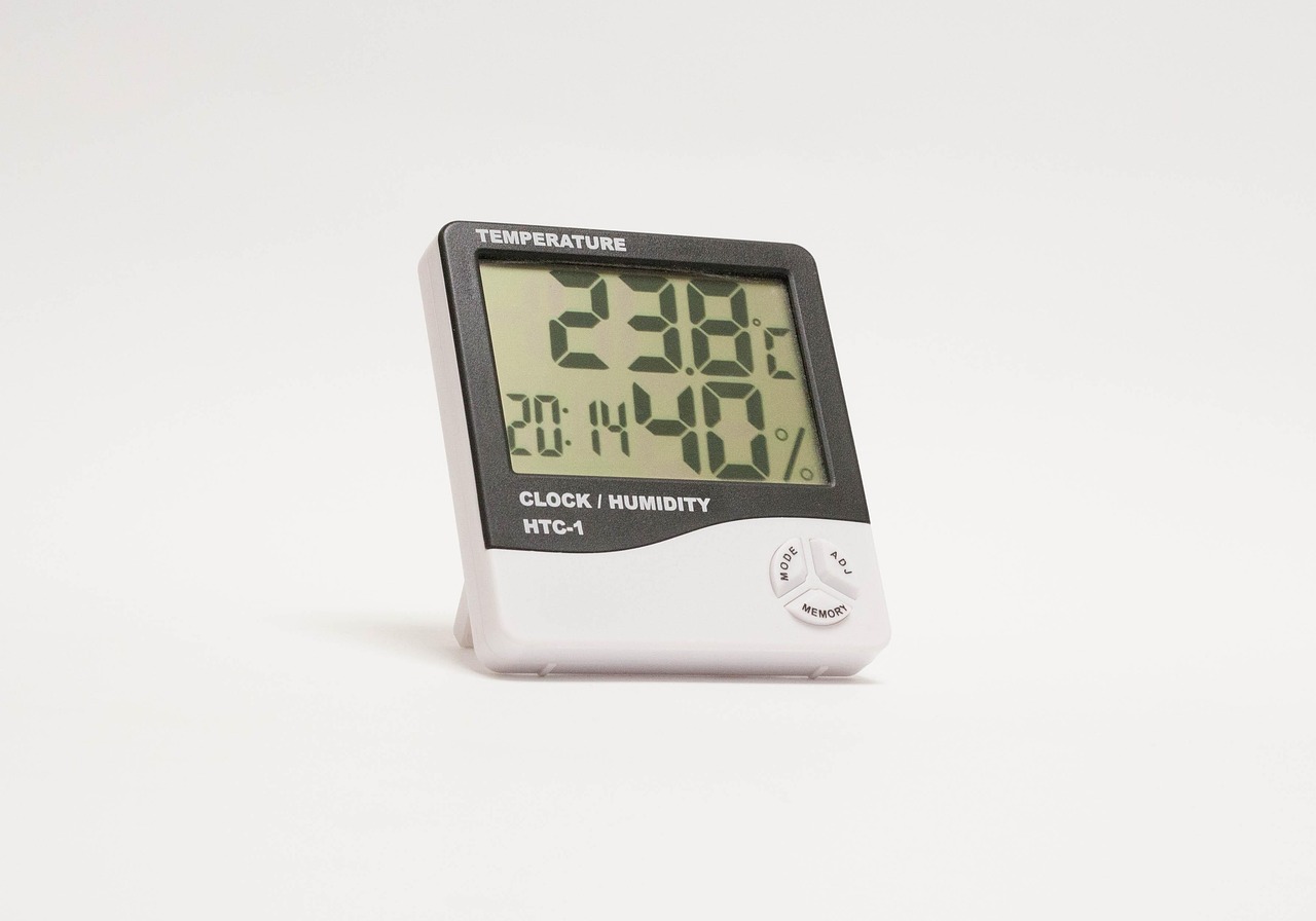 A hand holding a digital hygrometer reading indoor humidity levels inside a basement.