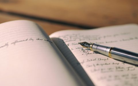 A person writing financial notes in a ledger with a pen.