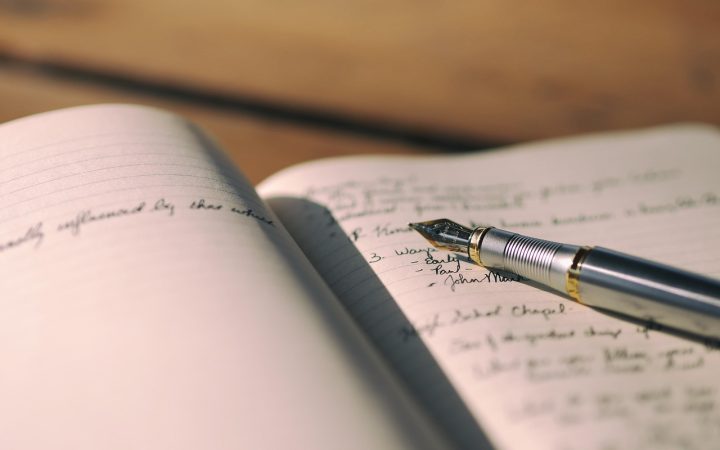A person writing financial notes in a ledger with a pen.