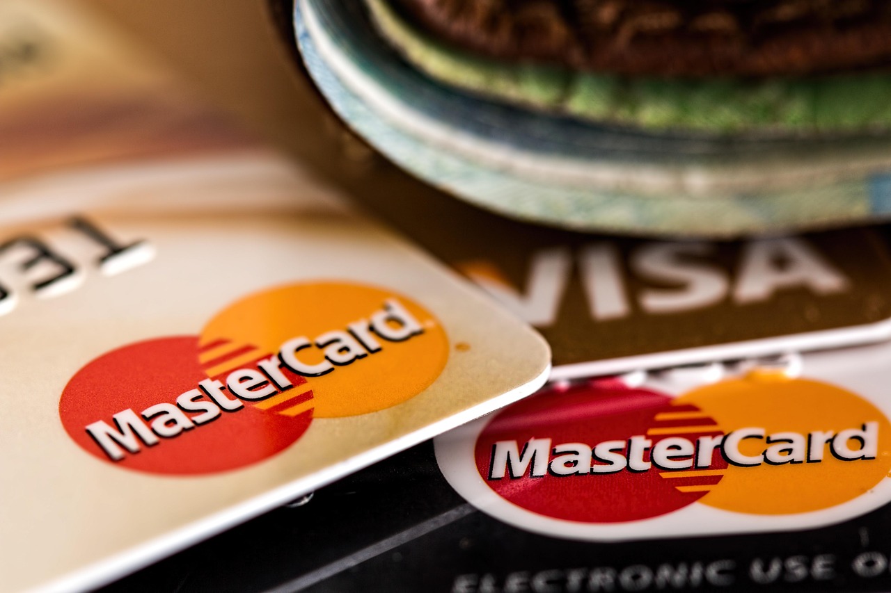 A person cross-referencing a digital banking app with printed credit card billing statements.