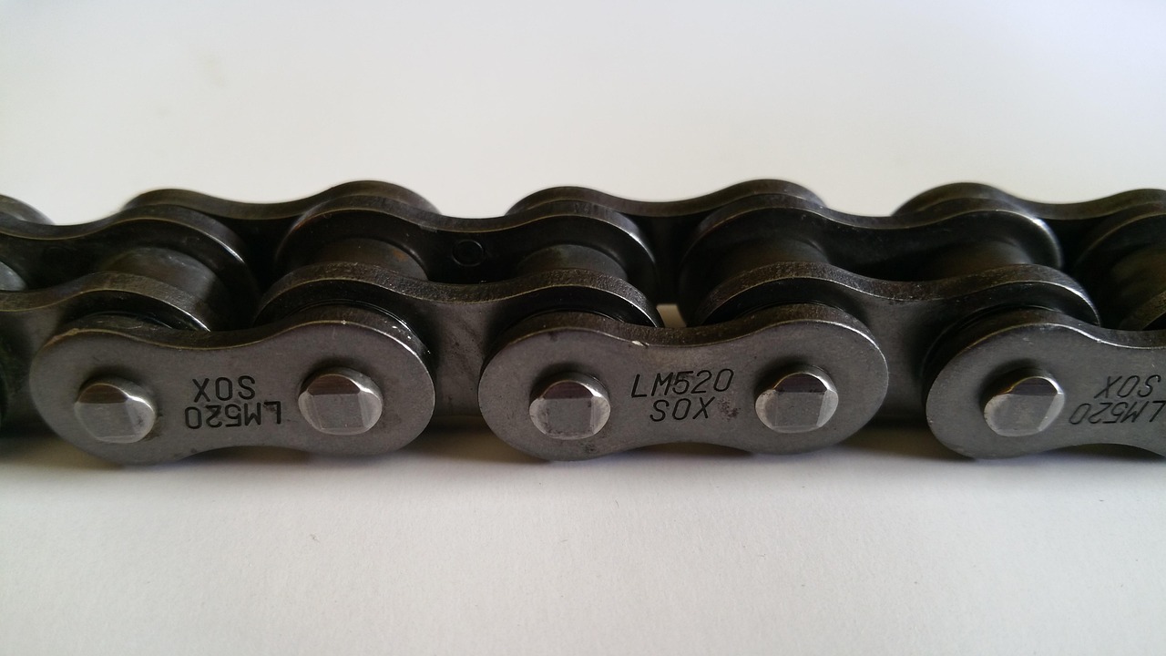 Hands checking the tension and wear on a motorcycle drive chain.