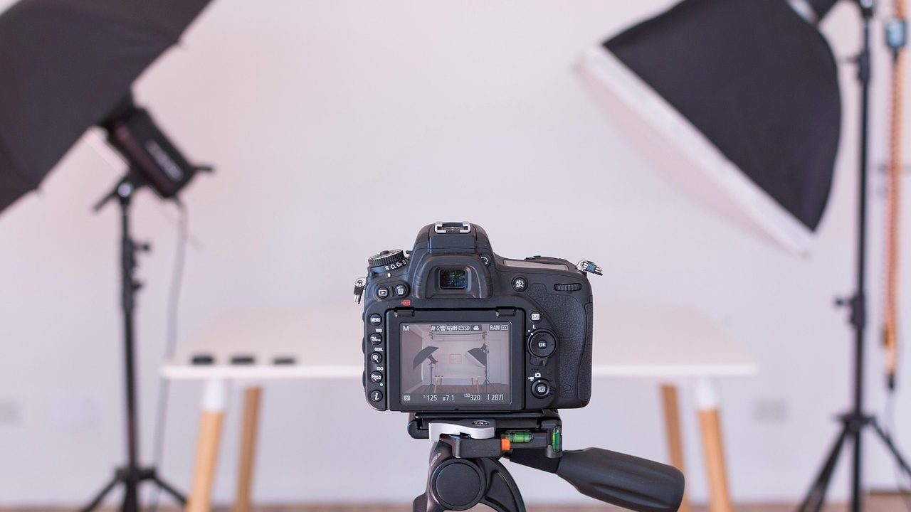 A modern home office desk featuring a mirrorless camera mounted on a tripod connected to a video capture card.