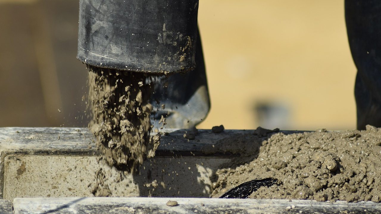 Close-up of a worker applying self-leveling polyurethane sealant into a concrete driveway expansion joint using a caulking gun.