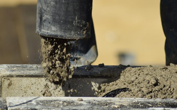 Close-up of a worker applying self-leveling polyurethane sealant into a concrete driveway expansion joint using a caulking gun.
