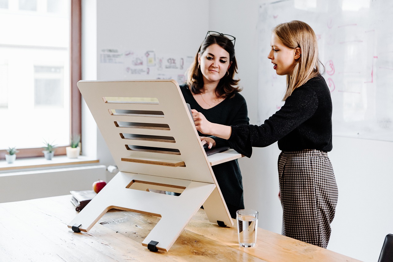 An office worker adjusting the angle and height of an articulated copyholder arm on a wooden desk.