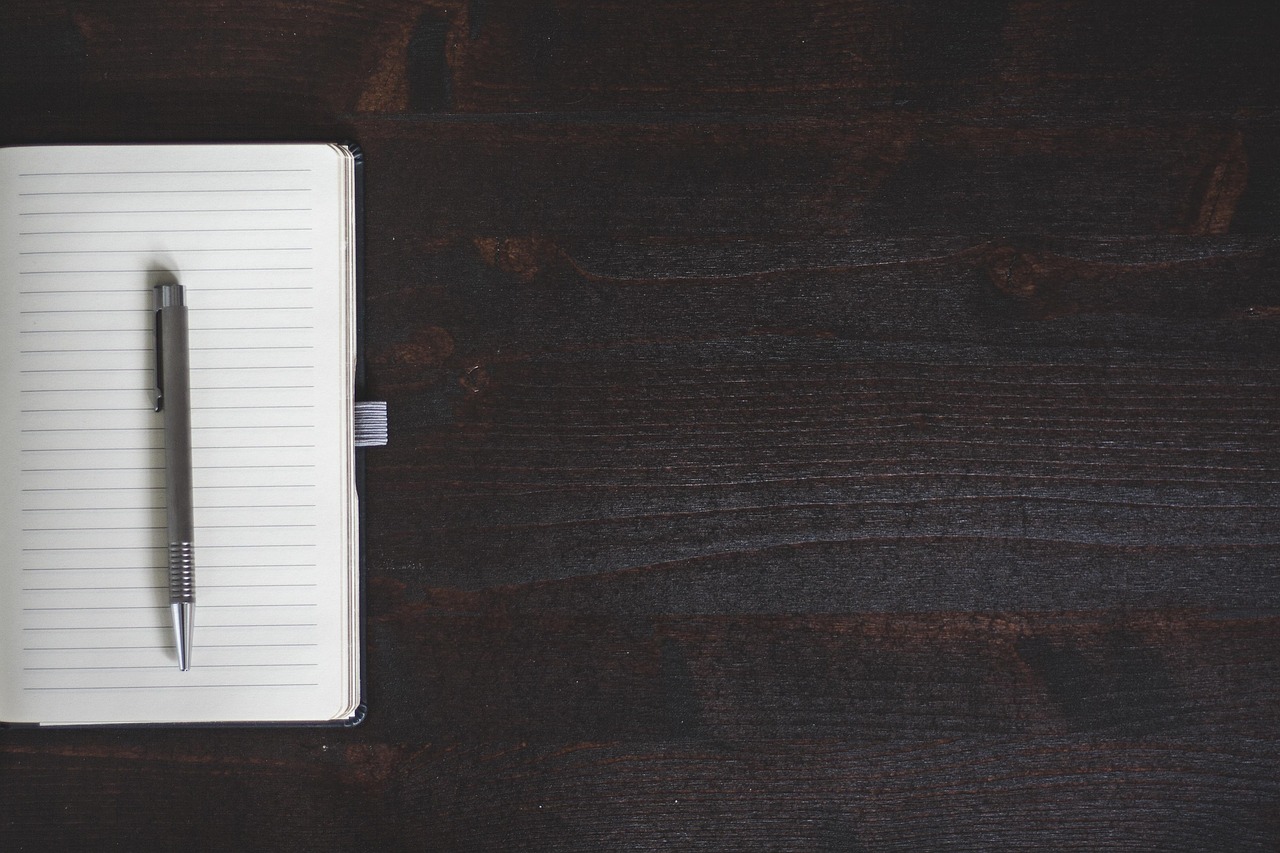 A clean open notebook with a pen on a minimalist wooden desk.