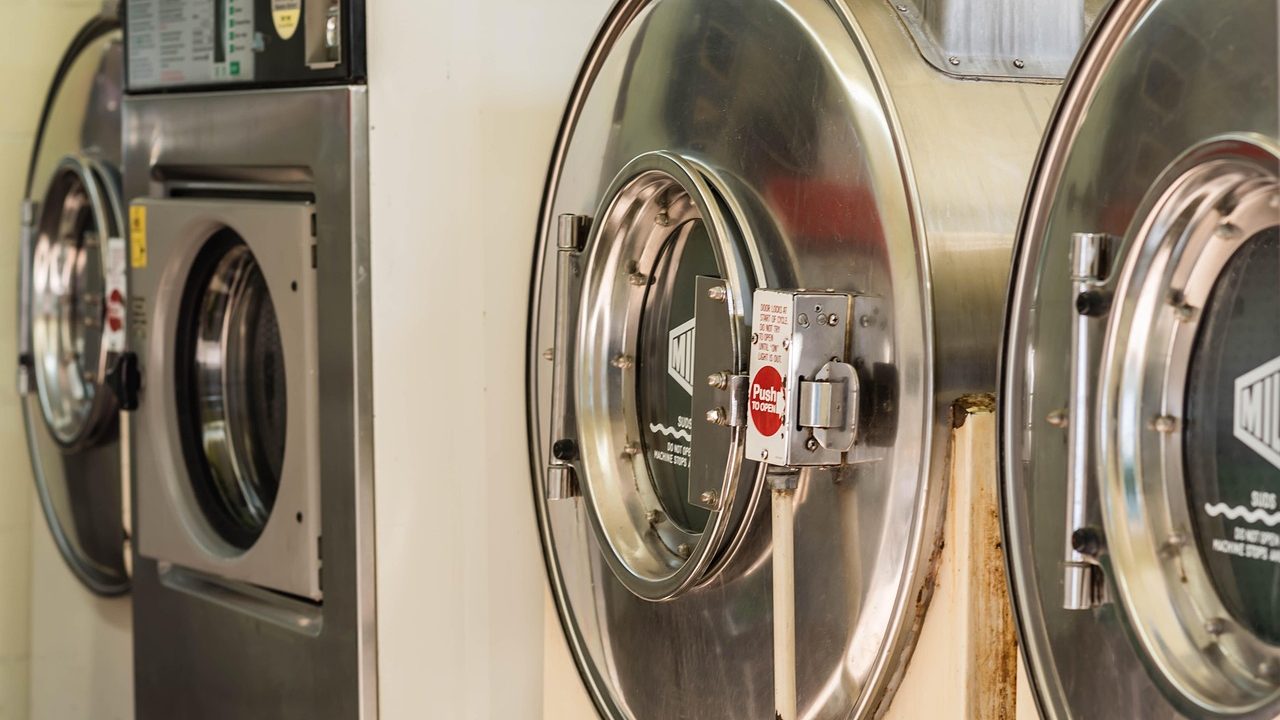 An appliance repair technician using tools on the back of an open clothes dryer.