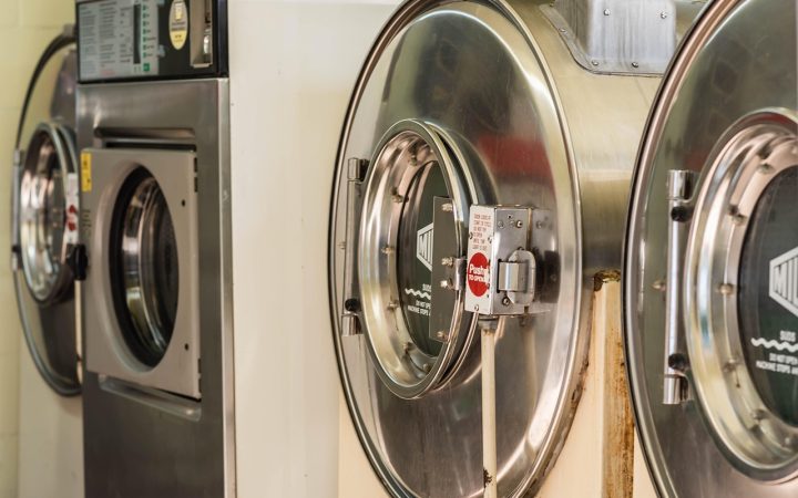 An appliance repair technician using tools on the back of an open clothes dryer.