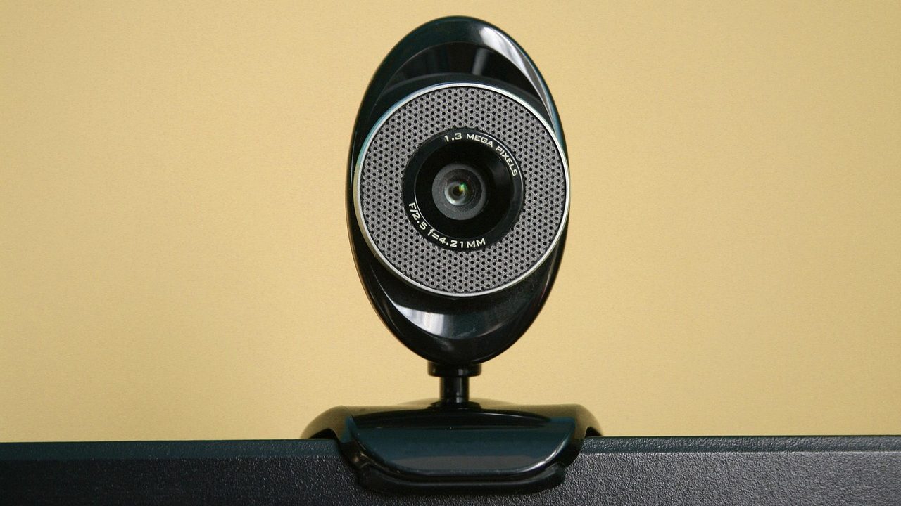 A remote professional carefully adjusting an external webcam mounted on a computer monitor.