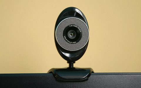 A remote professional carefully adjusting an external webcam mounted on a computer monitor.