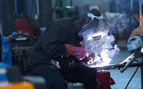 High school student wearing safety gear while practicing welding in a technical education workshop.