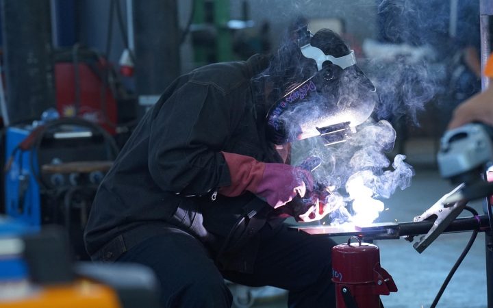 High school student wearing safety gear while practicing welding in a technical education workshop.