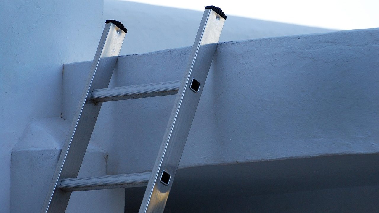 Homeowner cleaning leaves out of residential roof gutters using a ladder