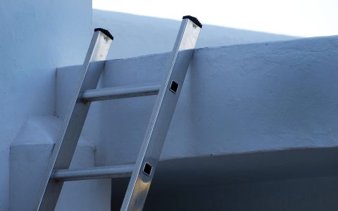 Homeowner cleaning leaves out of residential roof gutters using a ladder