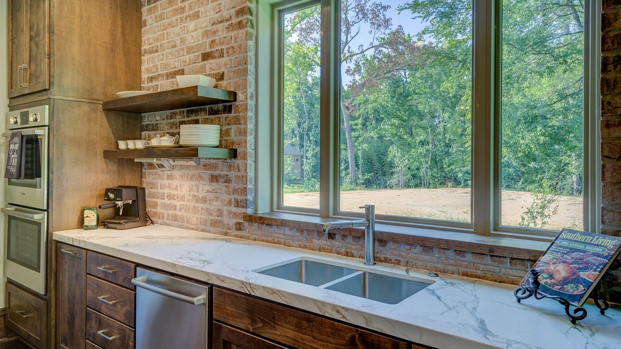 A compact white countertop dishwasher placed next to a stainless steel kitchen sink in a modern apartment.