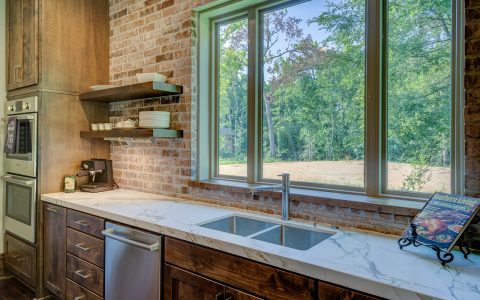 A compact white countertop dishwasher placed next to a stainless steel kitchen sink in a modern apartment.