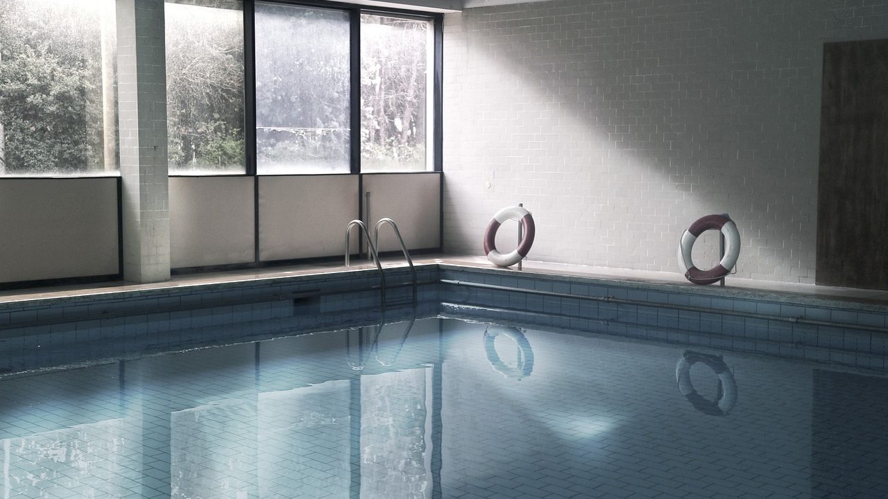 A robotic pool cleaner sitting on the tiled edge of a backyard swimming pool.