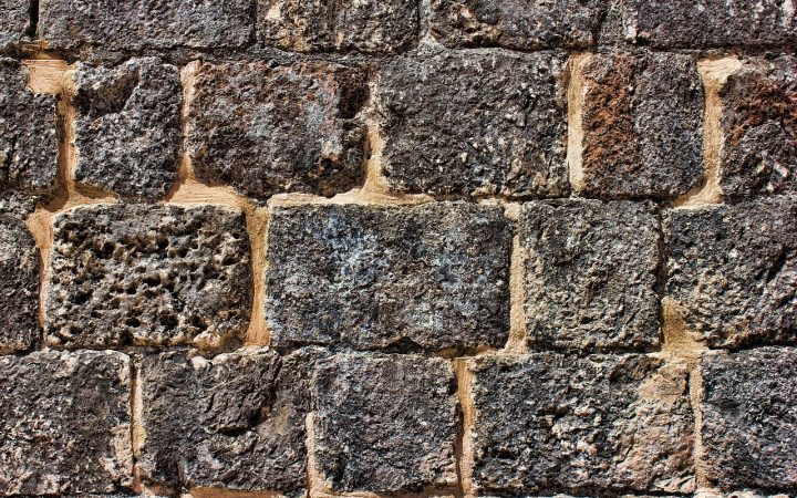 Homeowner inspecting a stone landscape retaining wall in a suburban yard
