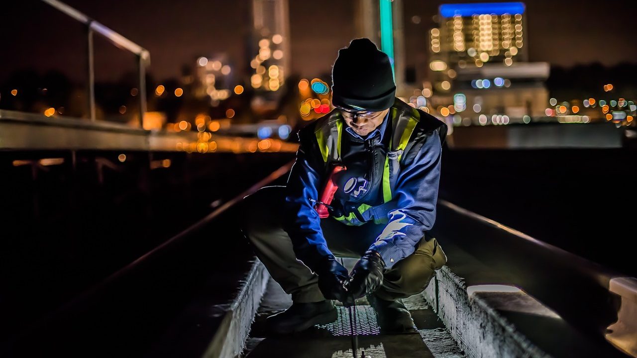 A technician wearing safety gear applying a cleaning solution to a shingle roof.
