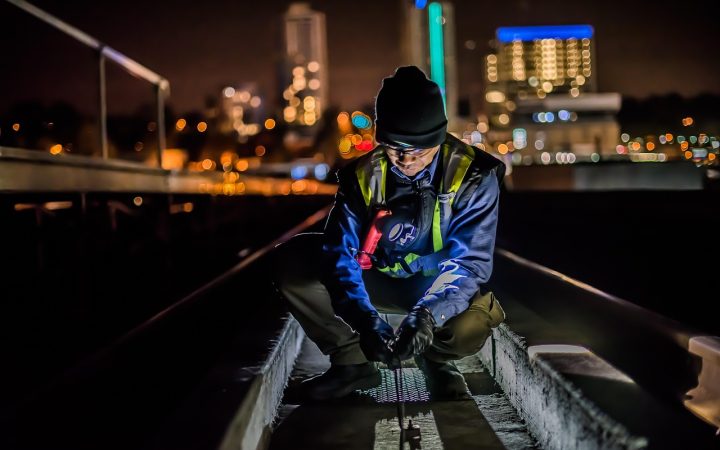 A technician wearing safety gear applying a cleaning solution to a shingle roof.
