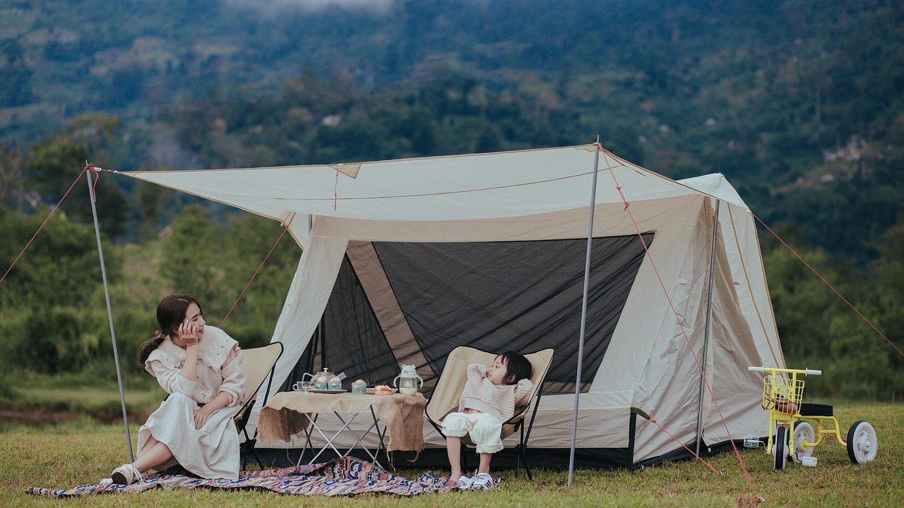 A family setting up a green camping tent at a public park campsite surrounded by trees.