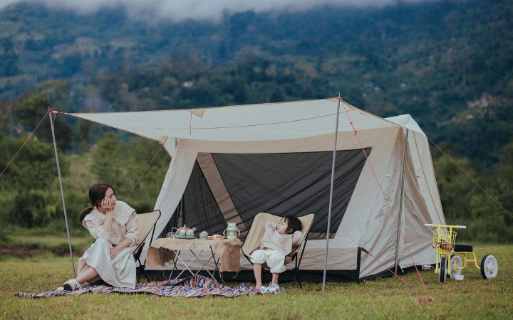 A family setting up a green camping tent at a public park campsite surrounded by trees.