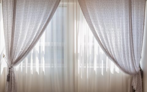 Heavy wool thermal curtain hanging over a wooden entryway interior in a cold home.