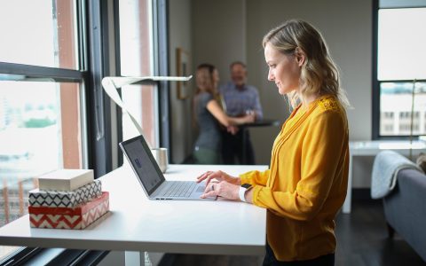 Remote worker typing on a laptop at a standing desk with a walking pad treadmill underneath.
