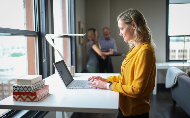 Remote worker typing on a laptop at a standing desk with a walking pad treadmill underneath.