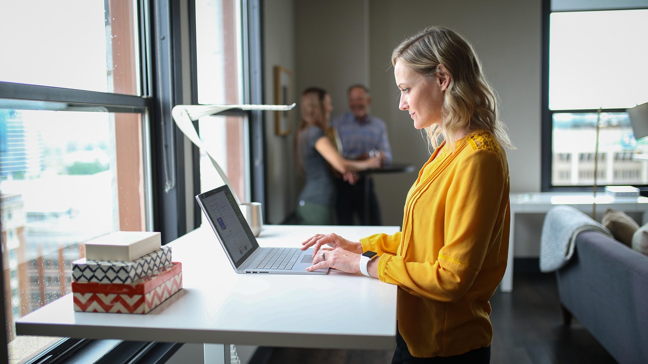 Remote worker typing on a laptop at a standing desk with a walking pad treadmill underneath.