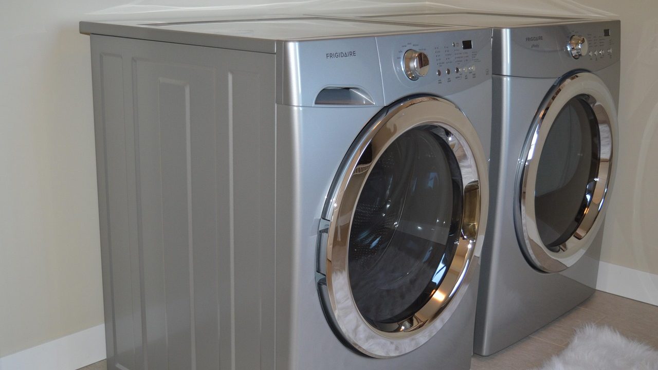 Front-load washer and dryer set installed on matching metal storage pedestals in a modern laundry room.
