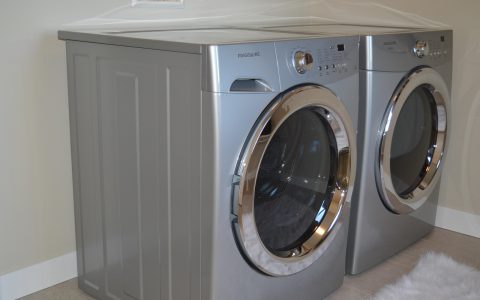 Front-load washer and dryer set installed on matching metal storage pedestals in a modern laundry room.