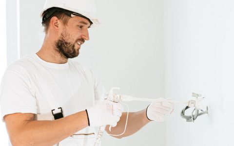 An electrician working on a ceiling bathroom exhaust fan installation.