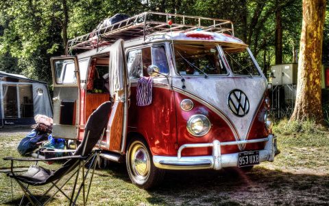 A popup camper fully set up at a scenic green campsite with its canvas sides and roof extended.