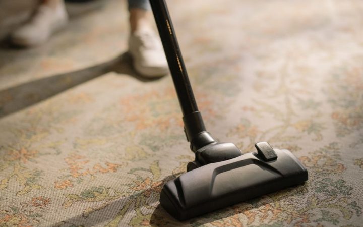 Professional carpet technician operating a commercial truck-mounted hot water extraction wand in a living room.