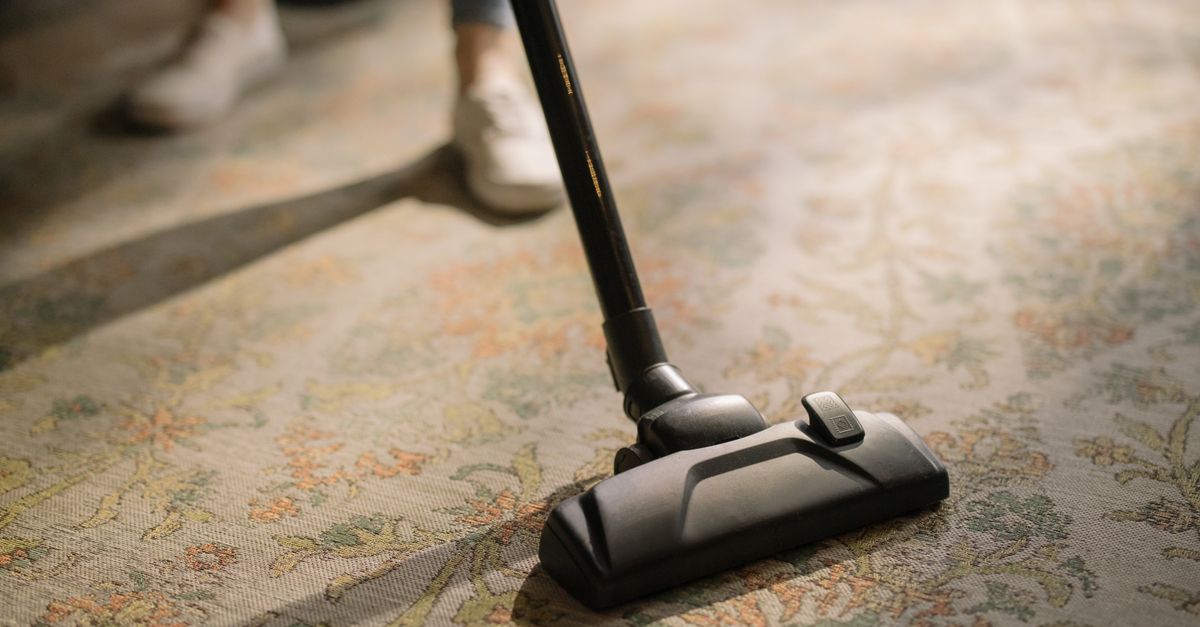 Professional carpet technician operating a commercial truck-mounted hot water extraction wand in a living room.
