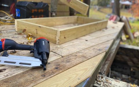 Homeowner inspecting wooden deck substructure framing with a flashlight