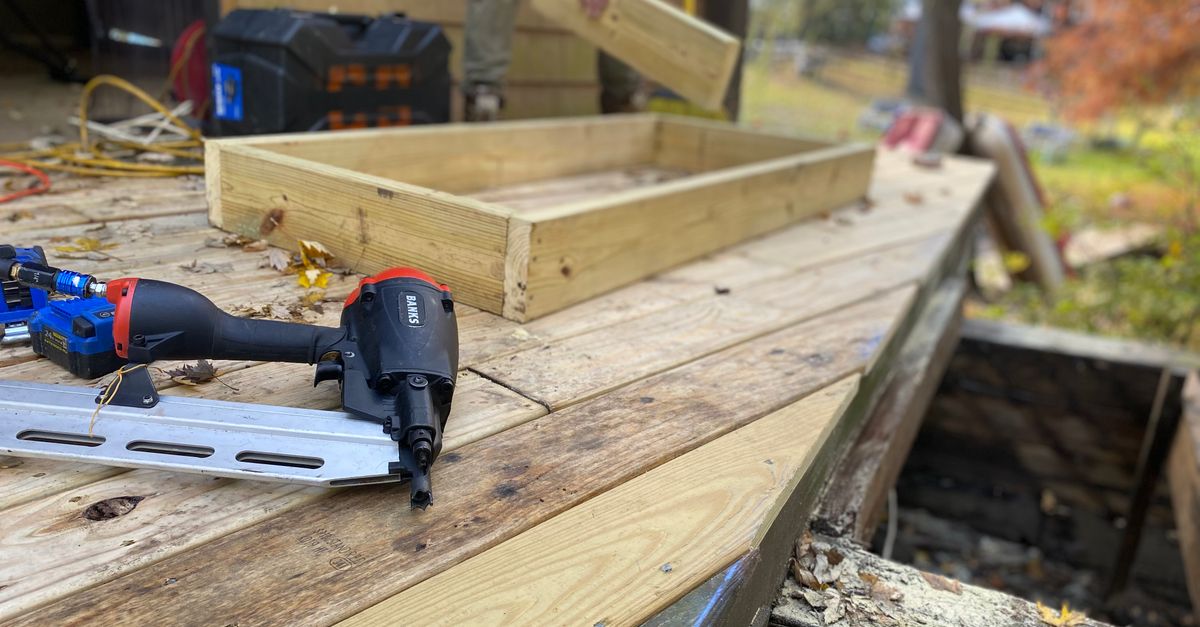 Homeowner inspecting wooden deck substructure framing with a flashlight
