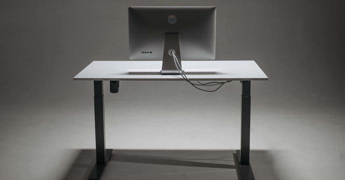 An office worker adjusting the height of a computer monitor on a wooden desktop shelf.