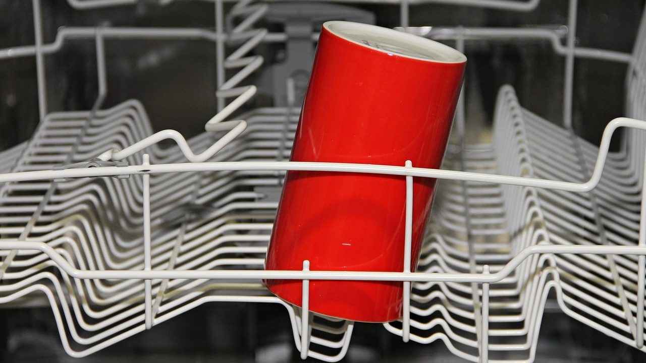 Close-up of a kitchen dishwasher lower rack removed with a technician checking the sump and drain area.