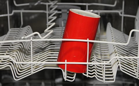 Close-up of a kitchen dishwasher lower rack removed with a technician checking the sump and drain area.