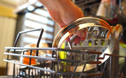 Person loading clean plates into a modern stainless steel dishwasher in a residential kitchen.