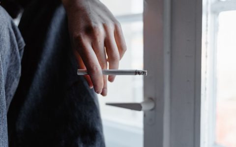 Homeowner performing an air leak test with a smoke pencil near a window frame.