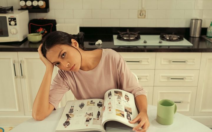 A woman looking tired and stressed while sitting at a kitchen table with papers.