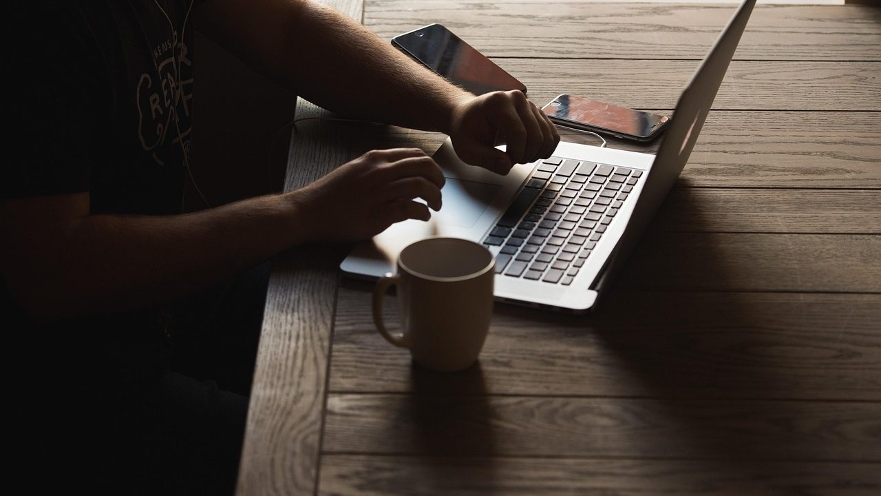 Person sitting at a wooden desk reviewing digital subscription bills on a laptop computer screen.