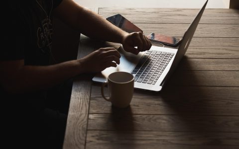 Person sitting at a wooden desk reviewing digital subscription bills on a laptop computer screen.