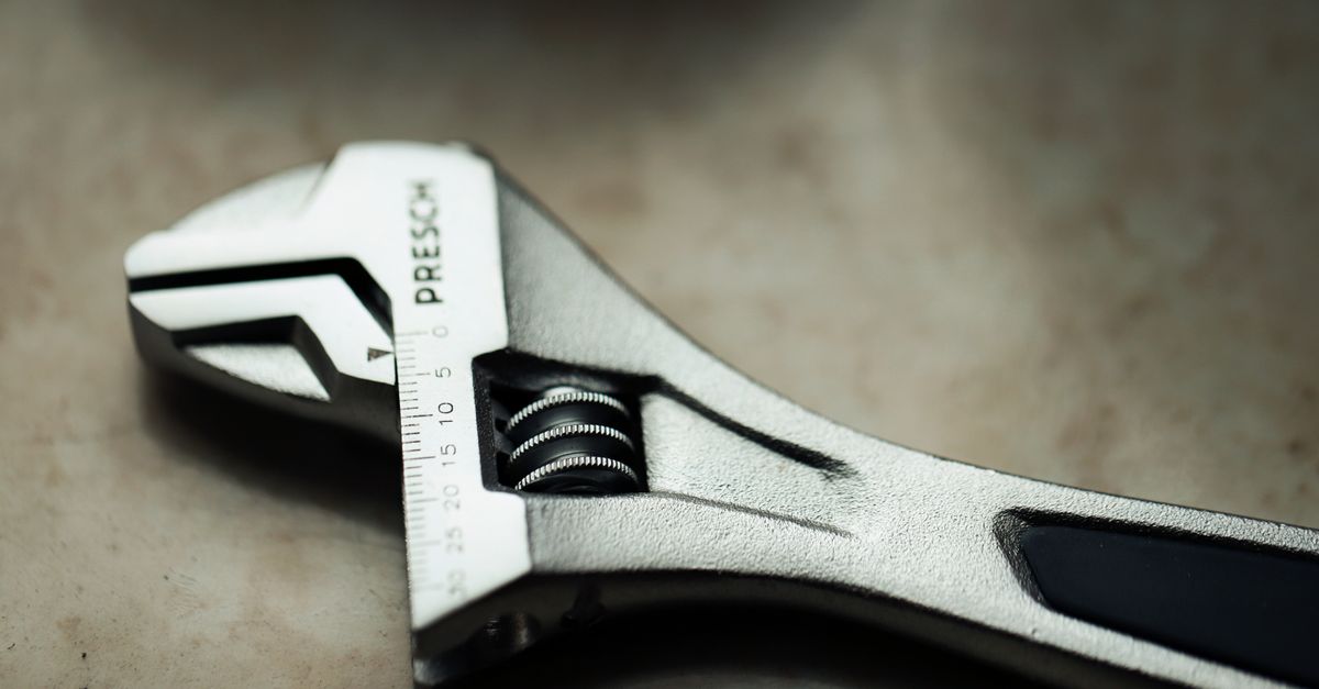 Close-up of a wrench tightening a metal connection under a toilet tank.