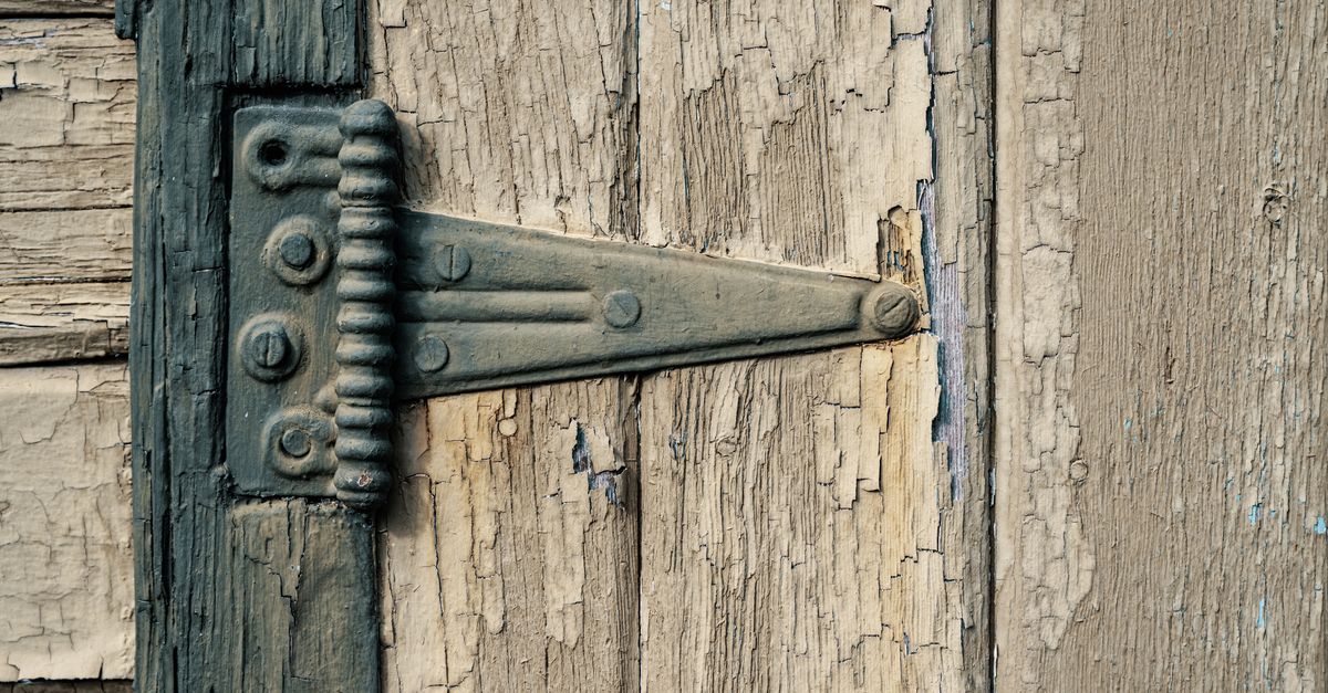 Close-up of a screwdriver adjusting hinge screws on an exterior door frame.